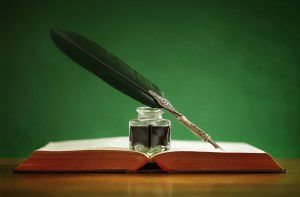 Quill pen and inkwell resting on an old book with green backgrou